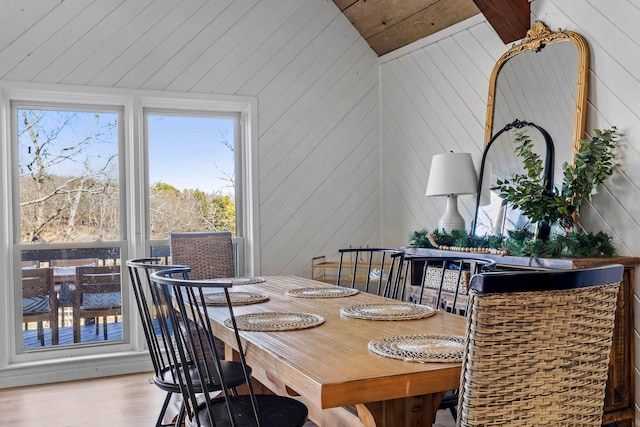 dining room with vaulted ceiling with beams, light hardwood / wood-style floors, and wooden walls