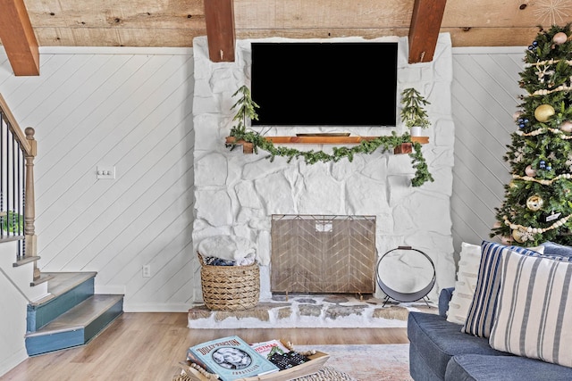 living room featuring beamed ceiling, light hardwood / wood-style flooring, a stone fireplace, and wood walls