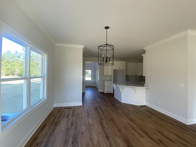 kitchen featuring dark wood-type flooring, white cabinets, crown molding, decorative light fixtures, and a breakfast bar area