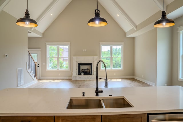 kitchen with a high end fireplace, light wood-type flooring, sink, decorative light fixtures, and high vaulted ceiling