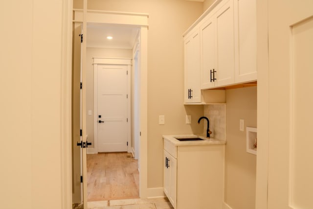 clothes washing area featuring cabinets, washer hookup, light hardwood / wood-style floors, and sink