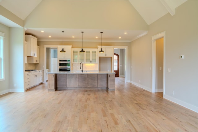 kitchen featuring a large island with sink, stainless steel double oven, hanging light fixtures, and lofted ceiling