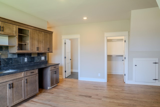 kitchen with decorative backsplash, light wood-type flooring, sink, and dark stone countertops