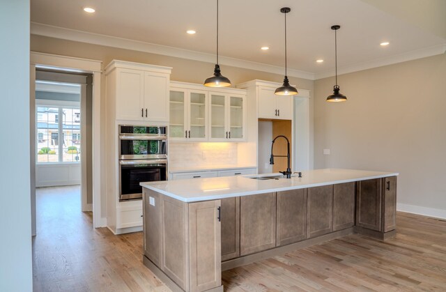 kitchen with white cabinetry, sink, stainless steel double oven, light hardwood / wood-style floors, and a center island with sink