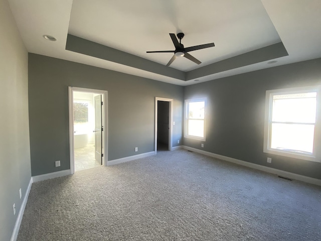 unfurnished bedroom with a tray ceiling, ensuite bath, ceiling fan, and carpet flooring