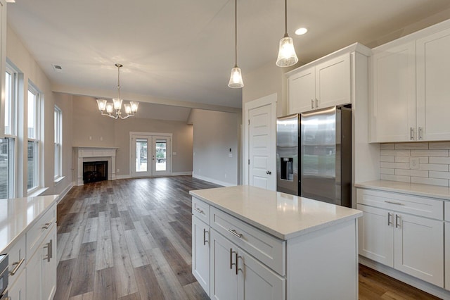 kitchen with backsplash, stainless steel fridge, white cabinets, and hanging light fixtures