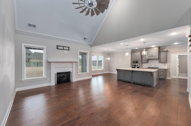 kitchen featuring gray cabinetry, high vaulted ceiling, ornamental molding, an island with sink, and pendant lighting