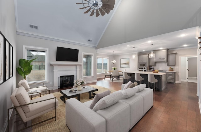 living room with high vaulted ceiling, crown molding, ceiling fan, dark hardwood / wood-style floors, and a fireplace