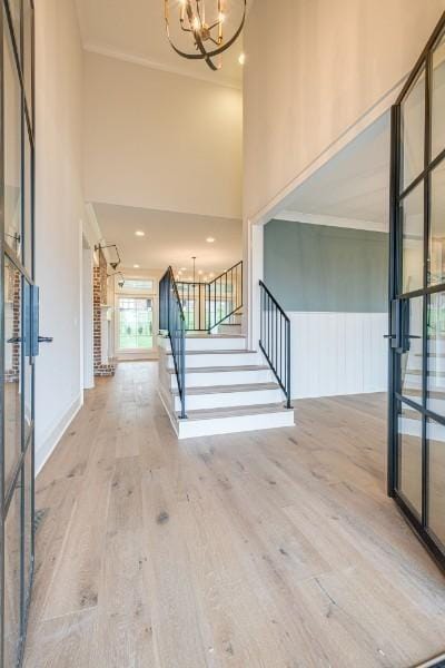 foyer entrance with an inviting chandelier, ornamental molding, a high ceiling, and hardwood / wood-style flooring