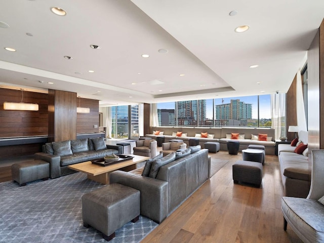 living room with hardwood / wood-style flooring, wooden walls, and a tray ceiling