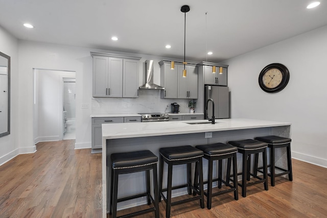 kitchen featuring sink, wall chimney exhaust hood, an island with sink, gray cabinets, and appliances with stainless steel finishes