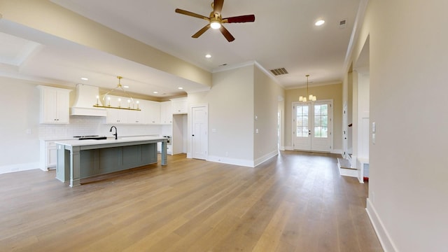 kitchen with white cabinetry, hanging light fixtures, a kitchen island with sink, ceiling fan with notable chandelier, and custom exhaust hood