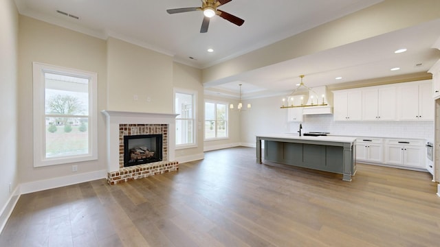 kitchen with pendant lighting, ceiling fan with notable chandelier, an island with sink, tasteful backsplash, and white cabinetry