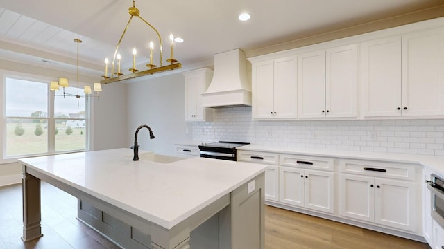 kitchen featuring a kitchen island with sink, hanging light fixtures, a notable chandelier, and custom exhaust hood