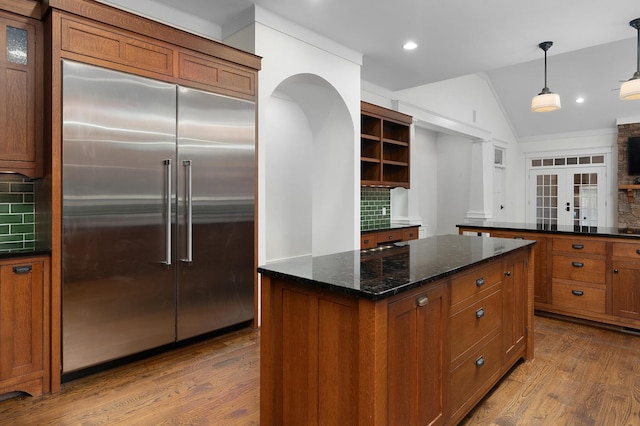 kitchen with french doors, tasteful backsplash, stainless steel built in refrigerator, dark stone counters, and decorative light fixtures