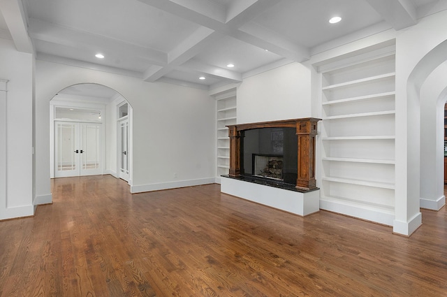 unfurnished living room featuring wood-type flooring, built in shelves, coffered ceiling, and beam ceiling