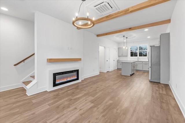 unfurnished living room with beam ceiling, sink, light wood-type flooring, and a notable chandelier