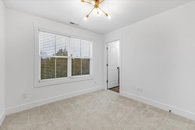 spare room featuring light carpet and an inviting chandelier