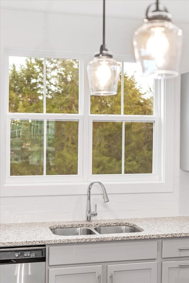 kitchen with dishwasher, sink, hanging light fixtures, light stone counters, and backsplash