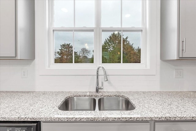 details featuring backsplash, gray cabinets, light stone counters, and sink