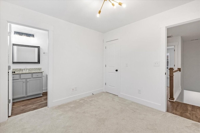 unfurnished bedroom with a chandelier, light carpet, sink, and ensuite bathroom