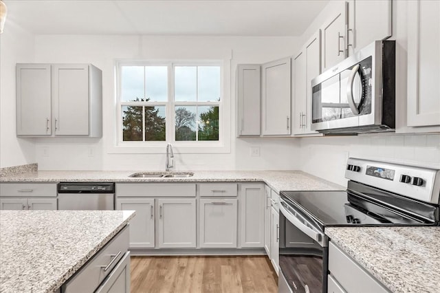 kitchen featuring appliances with stainless steel finishes, light wood-type flooring, light stone counters, gray cabinetry, and sink