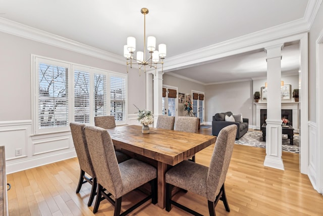 dining room featuring decorative columns, crown molding, light wood-type flooring, and a notable chandelier