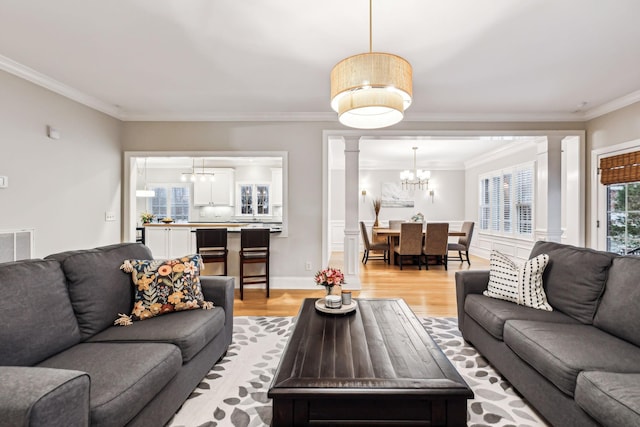 living room featuring ornate columns, crown molding, light hardwood / wood-style floors, and a notable chandelier