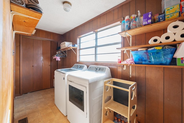 laundry area with a textured ceiling, washer and clothes dryer, and wood walls