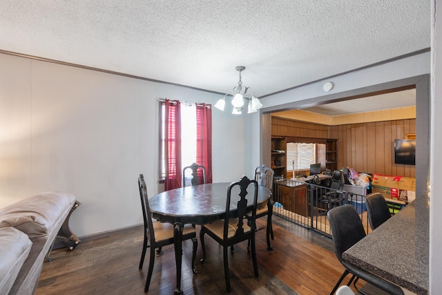 dining area featuring dark wood-type flooring, an inviting chandelier, wood walls, a textured ceiling, and ornamental molding