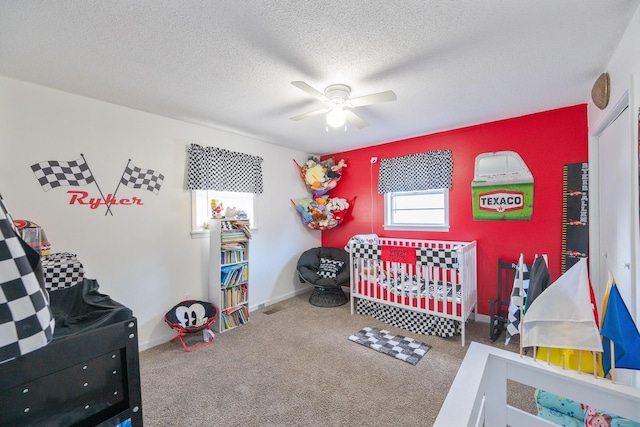 carpeted bedroom featuring ceiling fan, a textured ceiling, and a nursery area