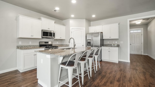 kitchen featuring light stone countertops, sink, stainless steel appliances, a kitchen island with sink, and white cabinets