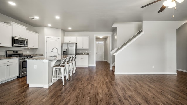 kitchen featuring a kitchen breakfast bar, light stone countertops, an island with sink, white cabinetry, and stainless steel appliances