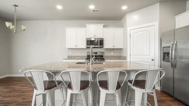 kitchen featuring dark hardwood / wood-style flooring, stainless steel appliances, an inviting chandelier, white cabinets, and an island with sink