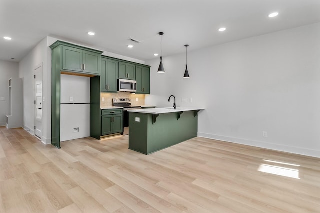 kitchen featuring a kitchen breakfast bar, green cabinets, light wood-type flooring, decorative light fixtures, and stainless steel appliances