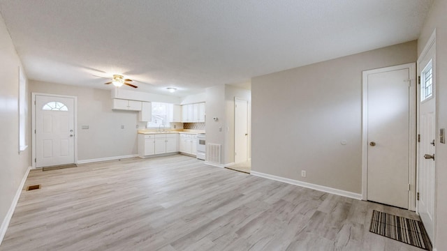 unfurnished living room featuring a textured ceiling, ceiling fan, sink, and light hardwood / wood-style flooring