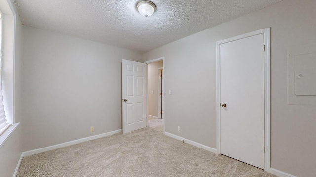 unfurnished bedroom featuring electric panel, a closet, light colored carpet, and a textured ceiling