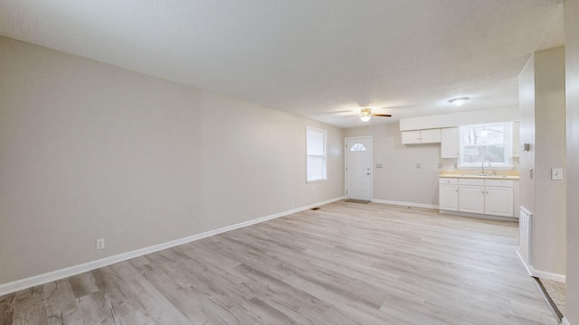 unfurnished living room featuring a textured ceiling, ceiling fan, light wood-type flooring, and sink