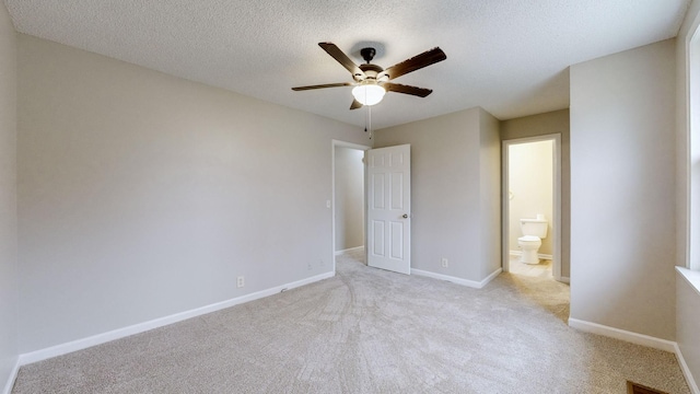 unfurnished bedroom featuring ceiling fan, light colored carpet, a textured ceiling, and ensuite bath