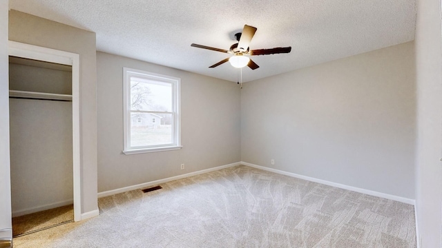 unfurnished bedroom with ceiling fan, light colored carpet, and a textured ceiling