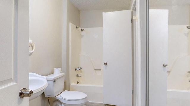 full bathroom featuring washtub / shower combination, a textured ceiling, toilet, and sink