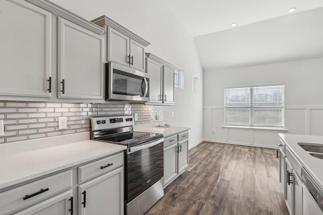 kitchen featuring gray cabinetry, dark hardwood / wood-style floors, lofted ceiling, decorative backsplash, and appliances with stainless steel finishes