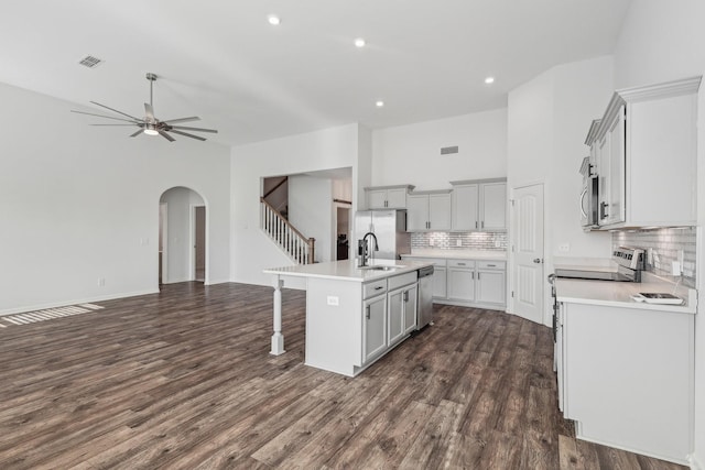 kitchen with dark hardwood / wood-style flooring, backsplash, ceiling fan, sink, and a center island with sink