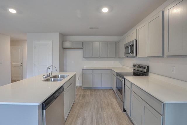 kitchen featuring sink, gray cabinets, a kitchen island with sink, appliances with stainless steel finishes, and light wood-type flooring