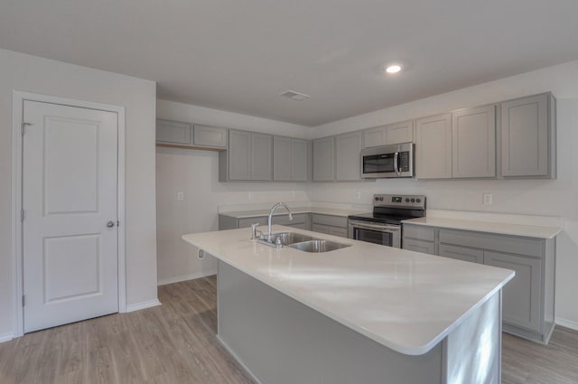 kitchen featuring sink, gray cabinets, an island with sink, appliances with stainless steel finishes, and light hardwood / wood-style floors