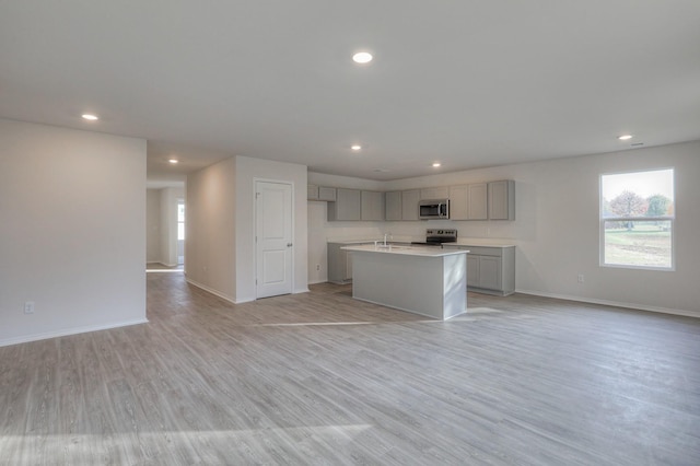 kitchen featuring gray cabinetry, a kitchen island with sink, light hardwood / wood-style floors, and appliances with stainless steel finishes