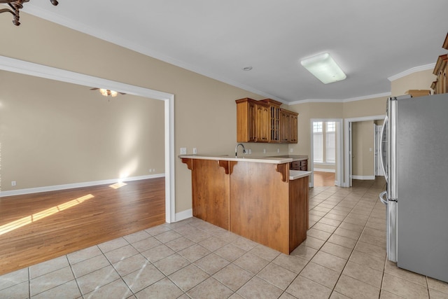 kitchen with a breakfast bar, crown molding, stainless steel fridge, light tile patterned flooring, and kitchen peninsula