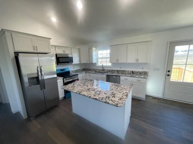 kitchen featuring white cabinetry, light stone countertops, a center island, stainless steel appliances, and dark hardwood / wood-style flooring