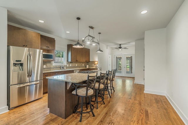 kitchen with light stone countertops, french doors, stainless steel appliances, decorative light fixtures, and decorative backsplash