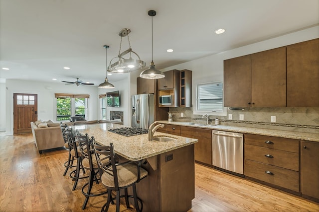 kitchen with ceiling fan, sink, an island with sink, a breakfast bar, and appliances with stainless steel finishes